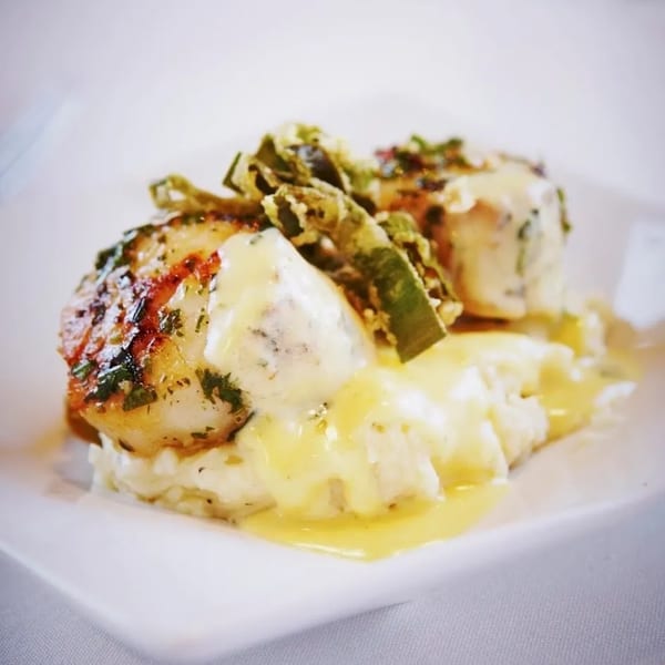 Seared scallops with asparagus and creamy sauce on a bed of mashed potatoes.