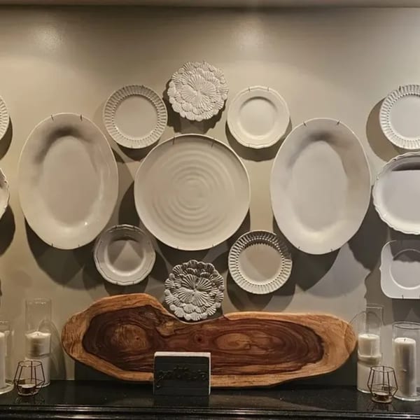 A wall decorated with various white plates and a wooden centerpiece with candles.