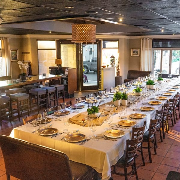 A long dining table set for a large group, with gold chargers and green plants as centerpieces.