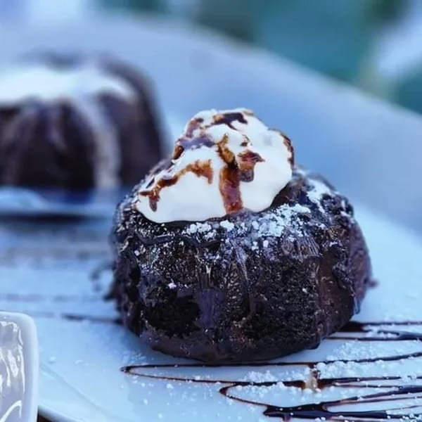 Chocolate lava cake with whipped cream, chocolate drizzle, and powdered sugar on a white plate.