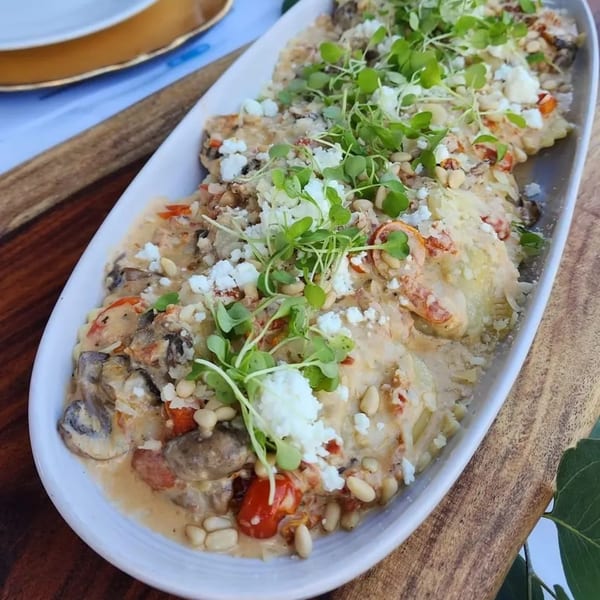 Creamy ravioli dish with mushrooms, tomatoes, feta, pine nuts, and microgreens on a white platter.
