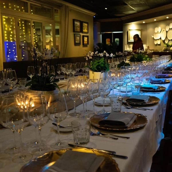 Long dining table set with wine glasses, gold plates, and candles, with a person in the background.