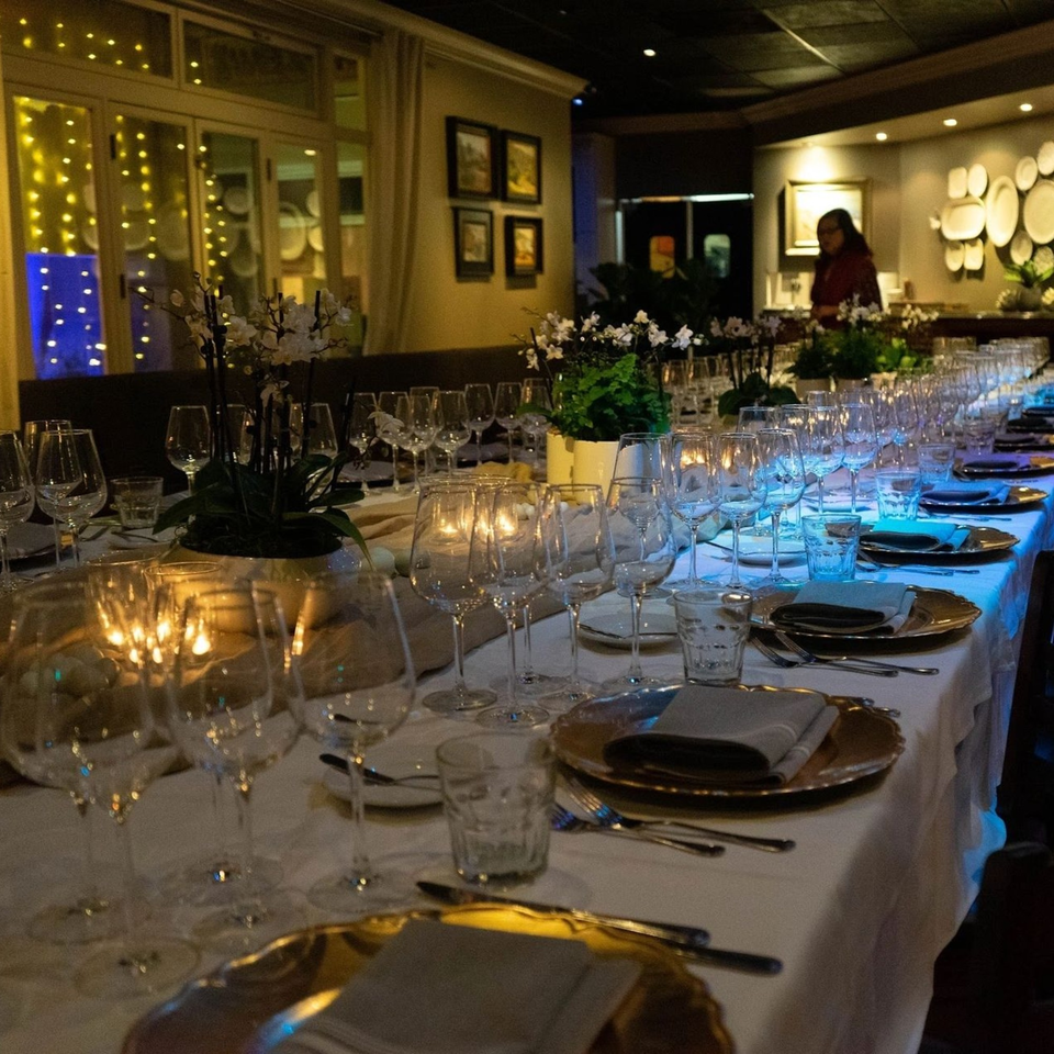 Long dining table set with wine glasses, gold plates, and candles, with a person in the background.