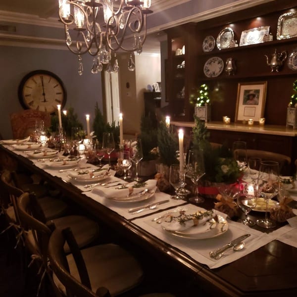 A long dining table set for a formal dinner with candles, festive greenery, and elegant place settings.
