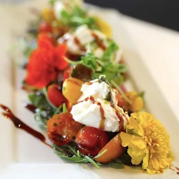 A vibrant caprese salad with burrata, cherry tomatoes, arugula, balsamic glaze, and edible flowers.