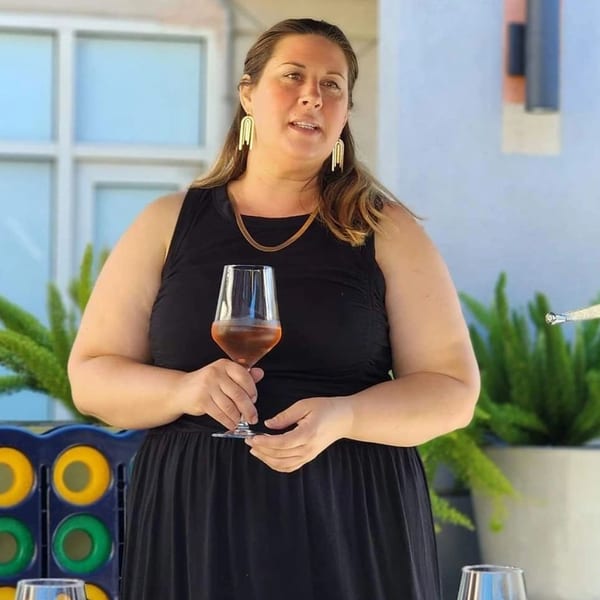 Chef Lindsay, a woman with long brown hair, holds a glass of rosé wine.
