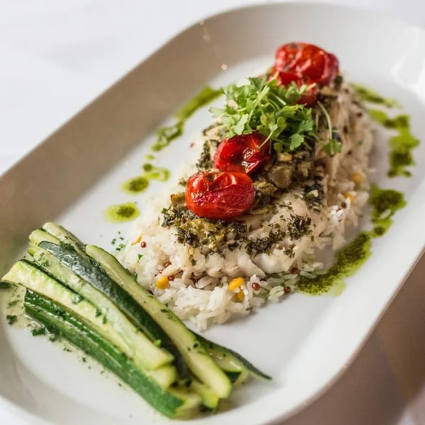 Nirvana by Chef Lindsay's American dish with fish, rice, roasted tomatoes, and zucchini on a white plate.