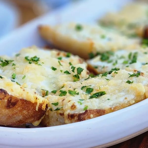 Close-up of cheesy garlic bread topped with fresh parsley, served in a white dish.