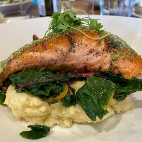Seared salmon with green sauce and herbs, served over mashed potatoes and sautéed greens.