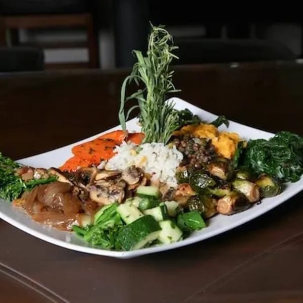A white plate filled with various vegetables, rice, and lentils, garnished with fresh herbs.