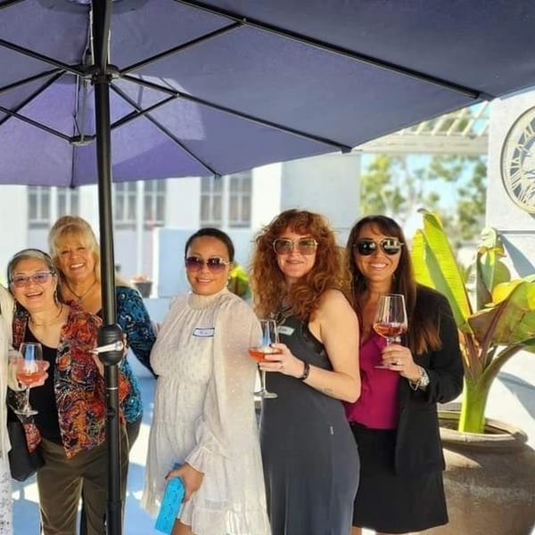 Five women smiling and holding wine glasses under a patio umbrella at Nirvana by Chef Lindsay.