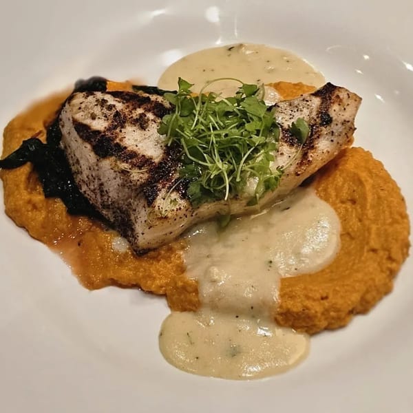 Grilled fish with microgreens, creamy sauce, and orange puree on a white plate.