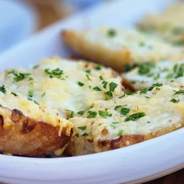 Close-up of golden-brown garlic bread topped with melted cheese and fresh green parsley on a white plate.