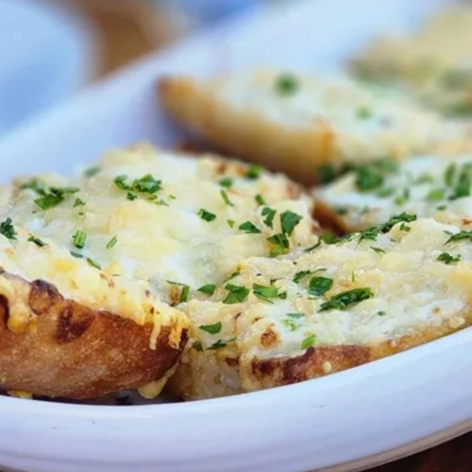 Close-up of golden-brown garlic bread topped with melted cheese and fresh green parsley on a white plate.