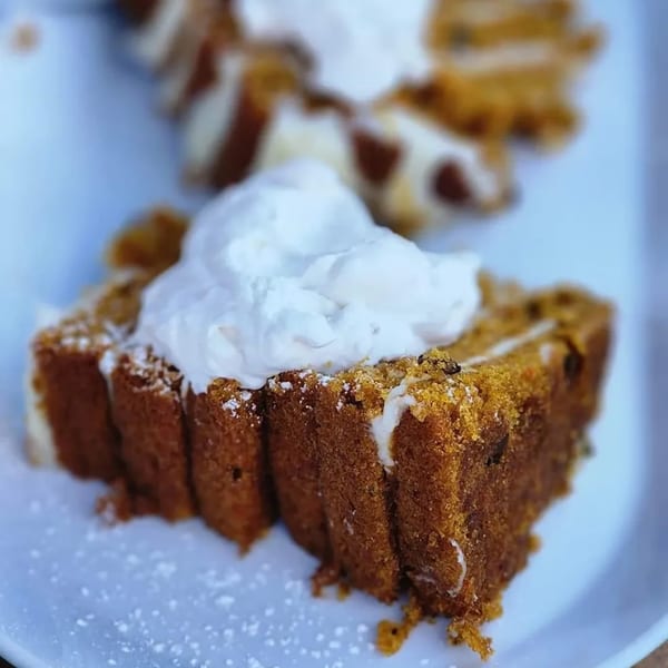 A slice of pumpkin bread topped with whipped cream and powdered sugar on a white plate.
