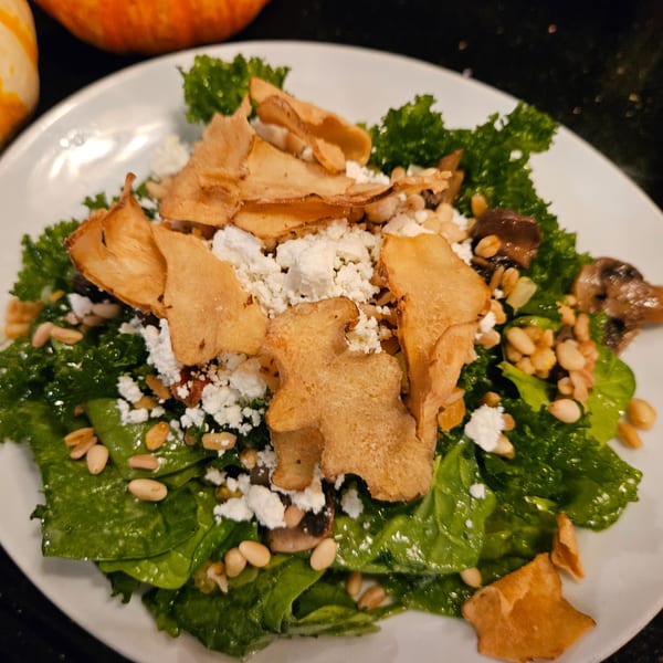 A vibrant green salad with crumbled feta, pine nuts, mushrooms, and crispy fried wontons on a white plate.