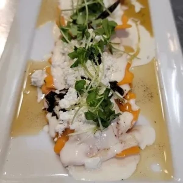 A gourmet dish featuring scallops, butternut squash, and microgreens, drizzled with sauce on a white plate.