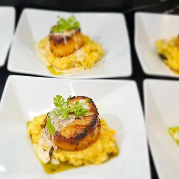 Seared scallops on creamy risotto, garnished with fresh herbs and a drizzle of green oil.