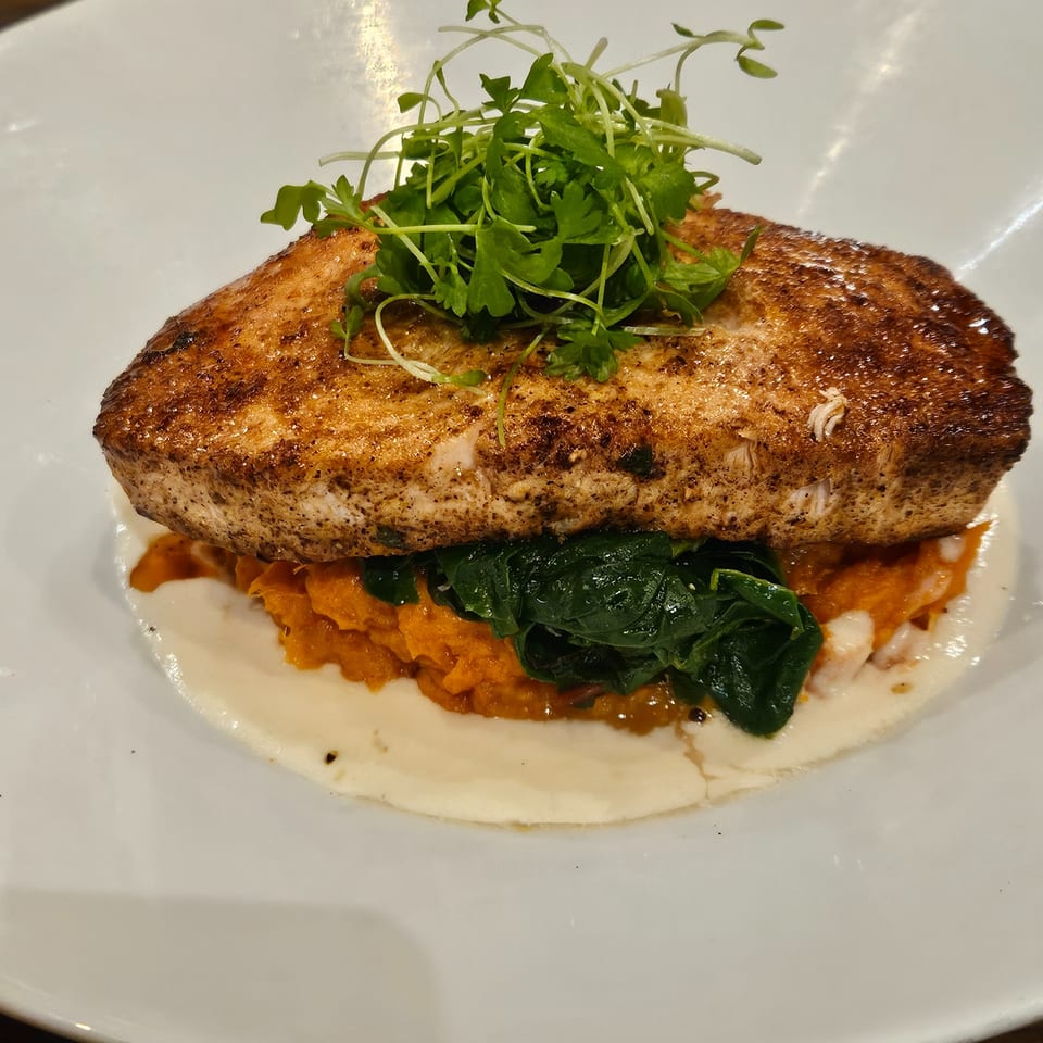 Seared fish fillet topped with microgreens, served over mashed sweet potatoes and spinach.