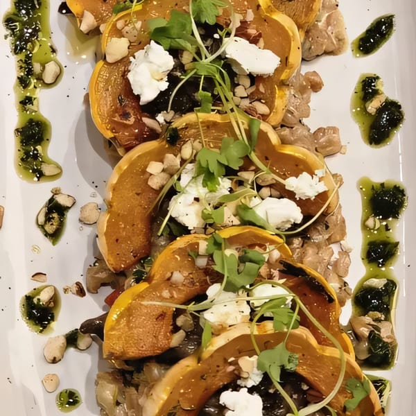 Roasted butternut squash with goat cheese, nuts, and herbs, drizzled with green sauce.
